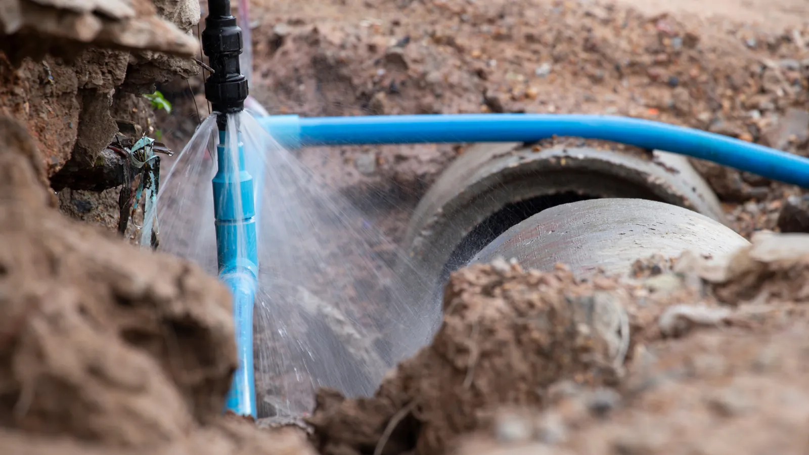 Burst water pipe spraying water in an excavated trench, an emergency plumbing call-out