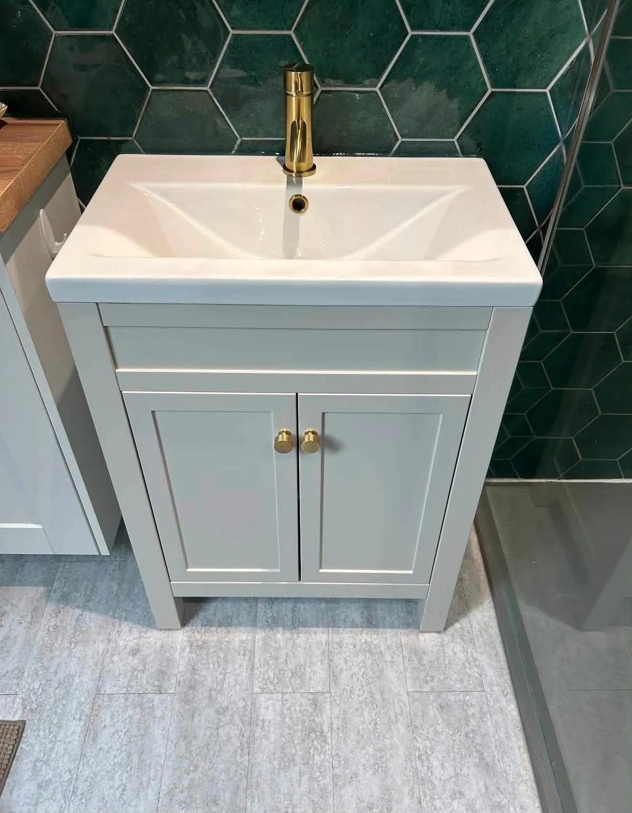 Freestanding basin vanity unit with brushed brass tap installed against green tiles